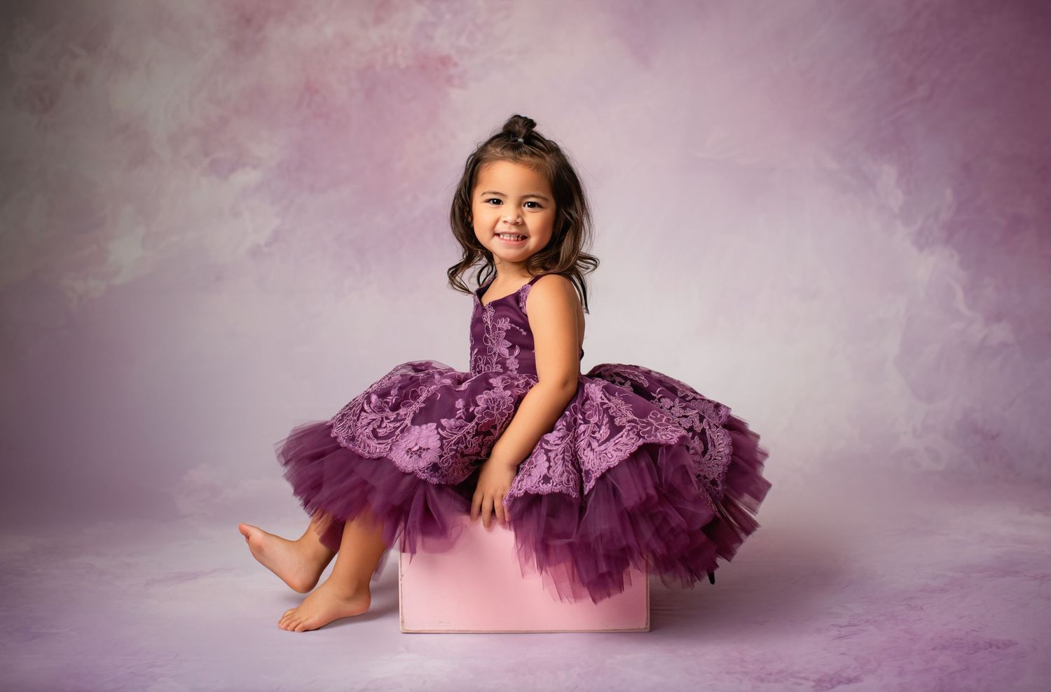 Purple tulle dress displayed on pink cube against dreamy pastel background.