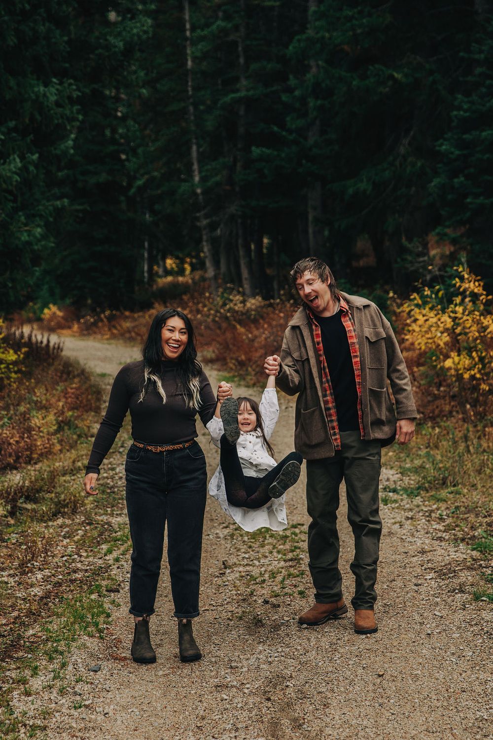 A family walks together on a forest path during autumn with fall foliage visible in the background.