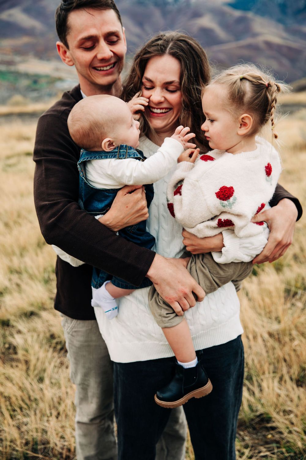 Family sharing joyful embraces and tender moments in a golden field during sunset.
