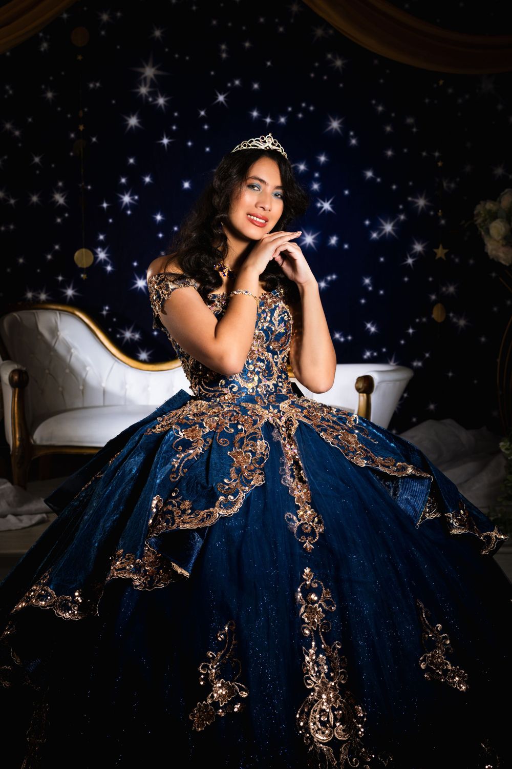 Glamorous quinceañera portrait with navy blue ball gown against starry background.