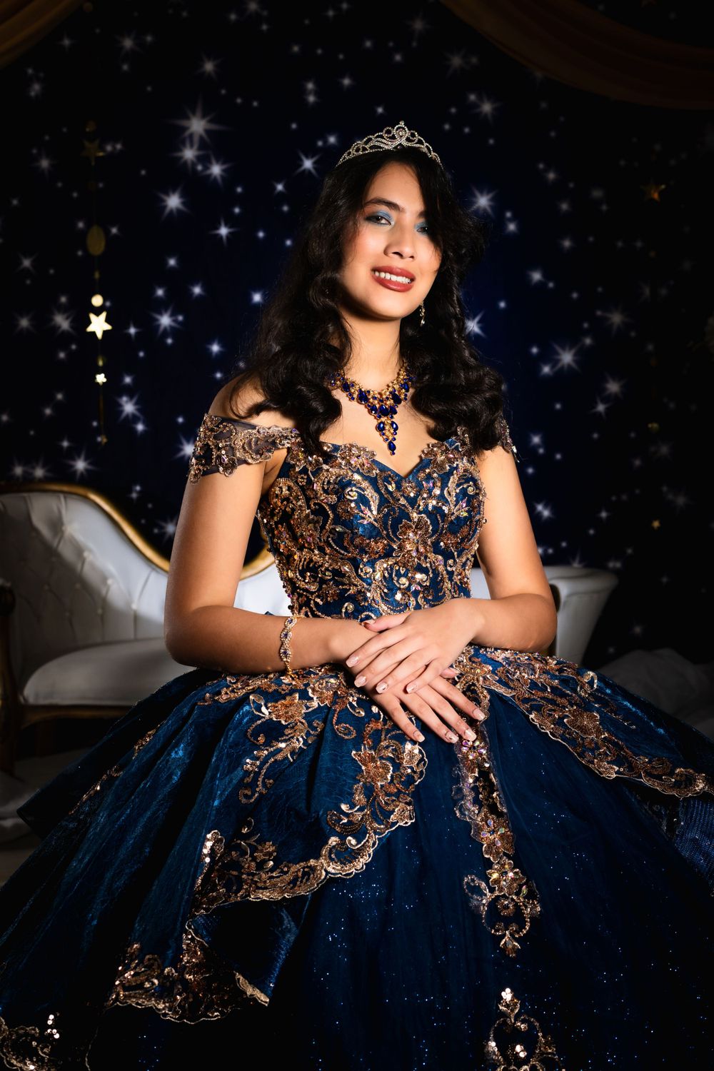 A stunning navy blue and gold quinceañera dress with intricate embroidery sparkles against a starry backdrop.