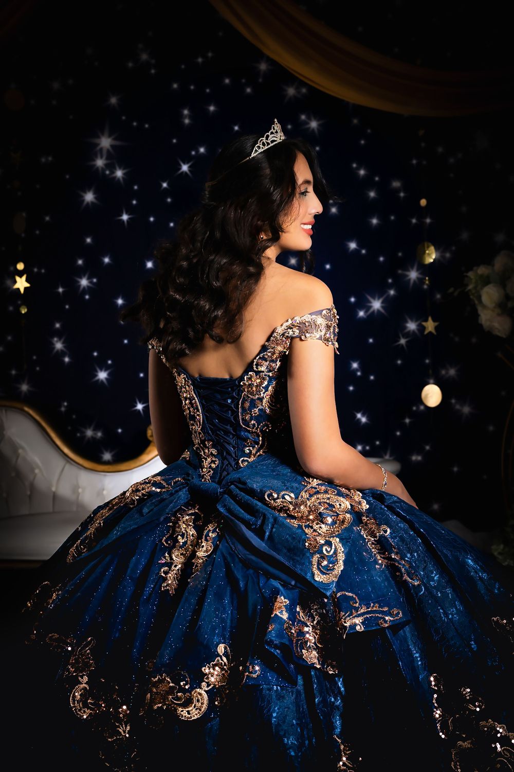 Side view of an ornate navy ball gown with copper embroidery against a starry backdrop.