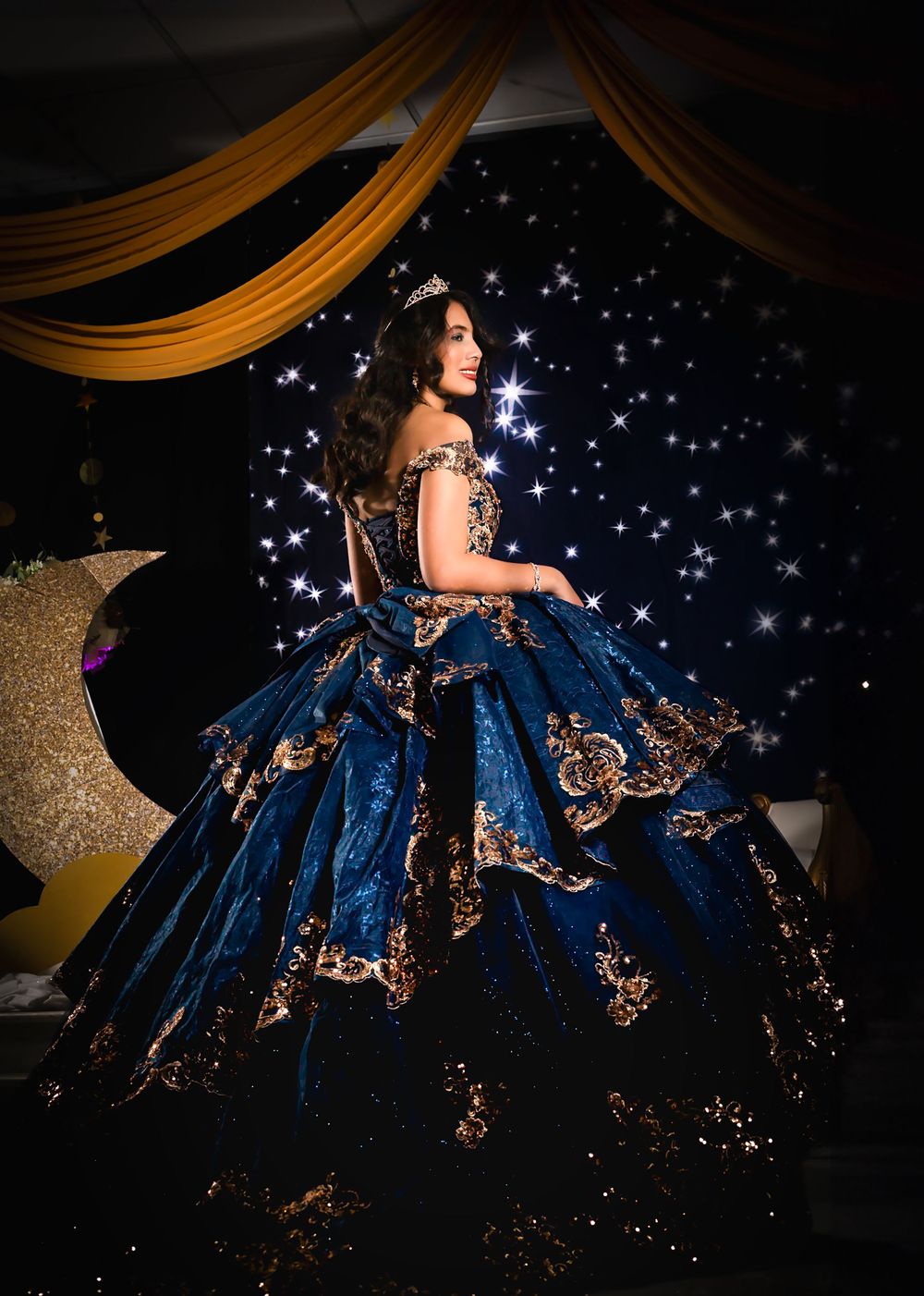 Full-length view of a navy ball gown with metallic appliques in a dramatic dark setting.