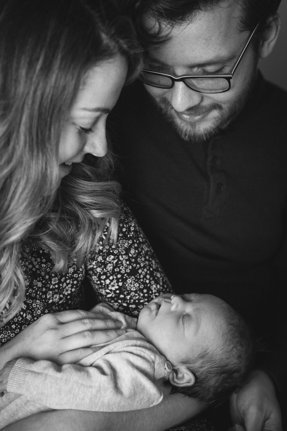 A tender black and white portrait of parents gazing lovingly at their newborn baby.