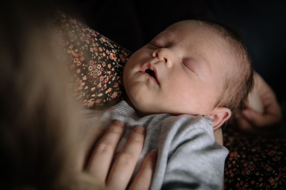Close-up of sleeping newborn against floral pattern in dramatic lighting.