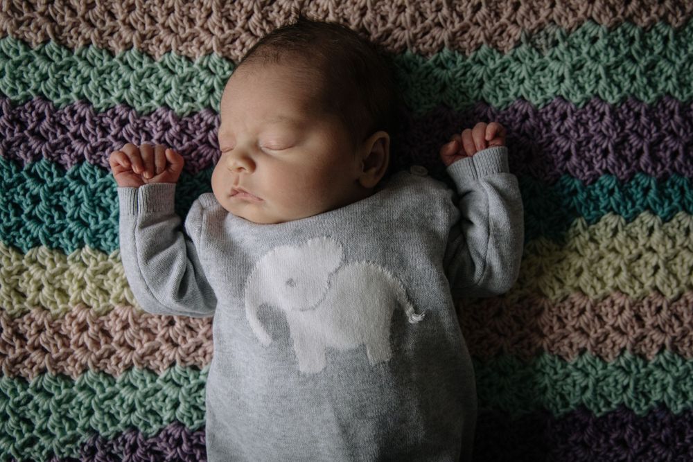 Sleeping newborn in grey outfit on colorful striped blanket.