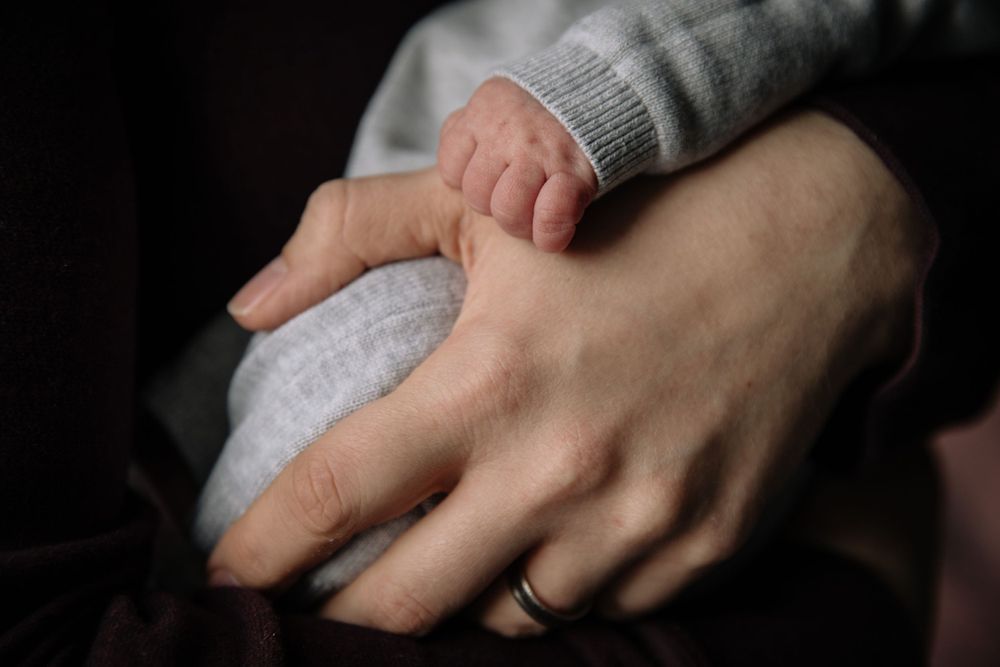 Close-up of hands gently cradling a baby in grey clothing.
