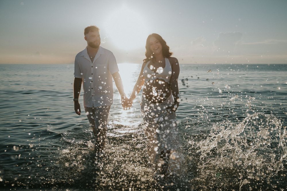 Couple holding hands walking through ocean waves at sunset on a beautiful beach.