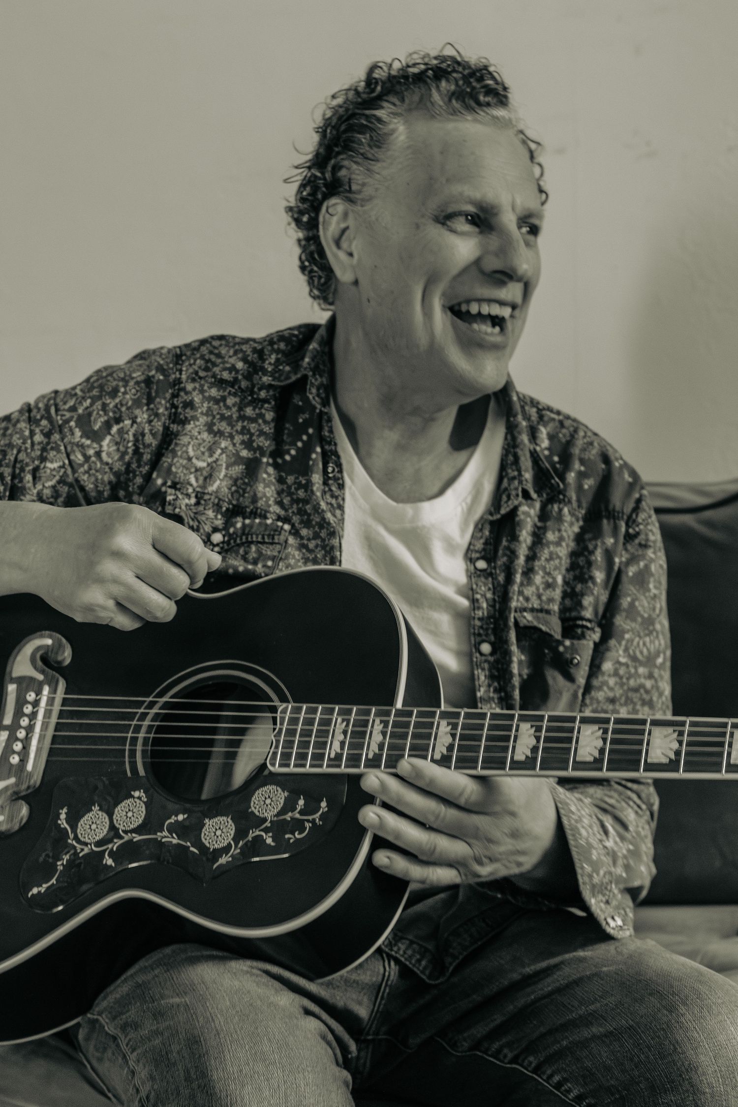 Portrait photography: black and white close-up of a man in a denim shirt laughing and playing an acoustic guitar