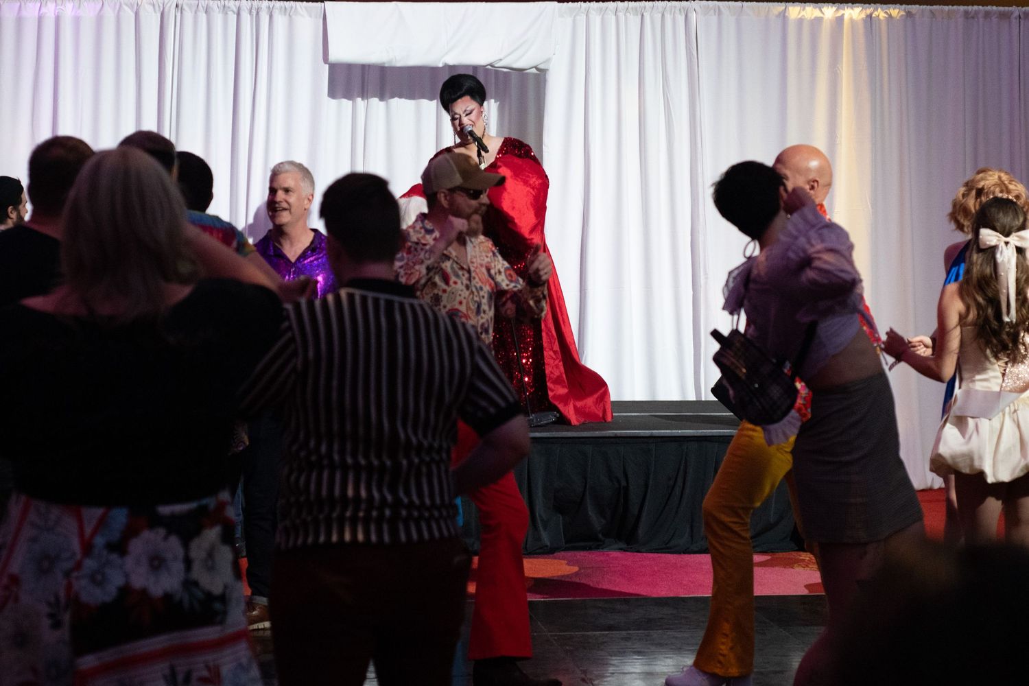 Performers and guests dancing on stage at a colorful theatrical event with dramatic red costume centerpiece.