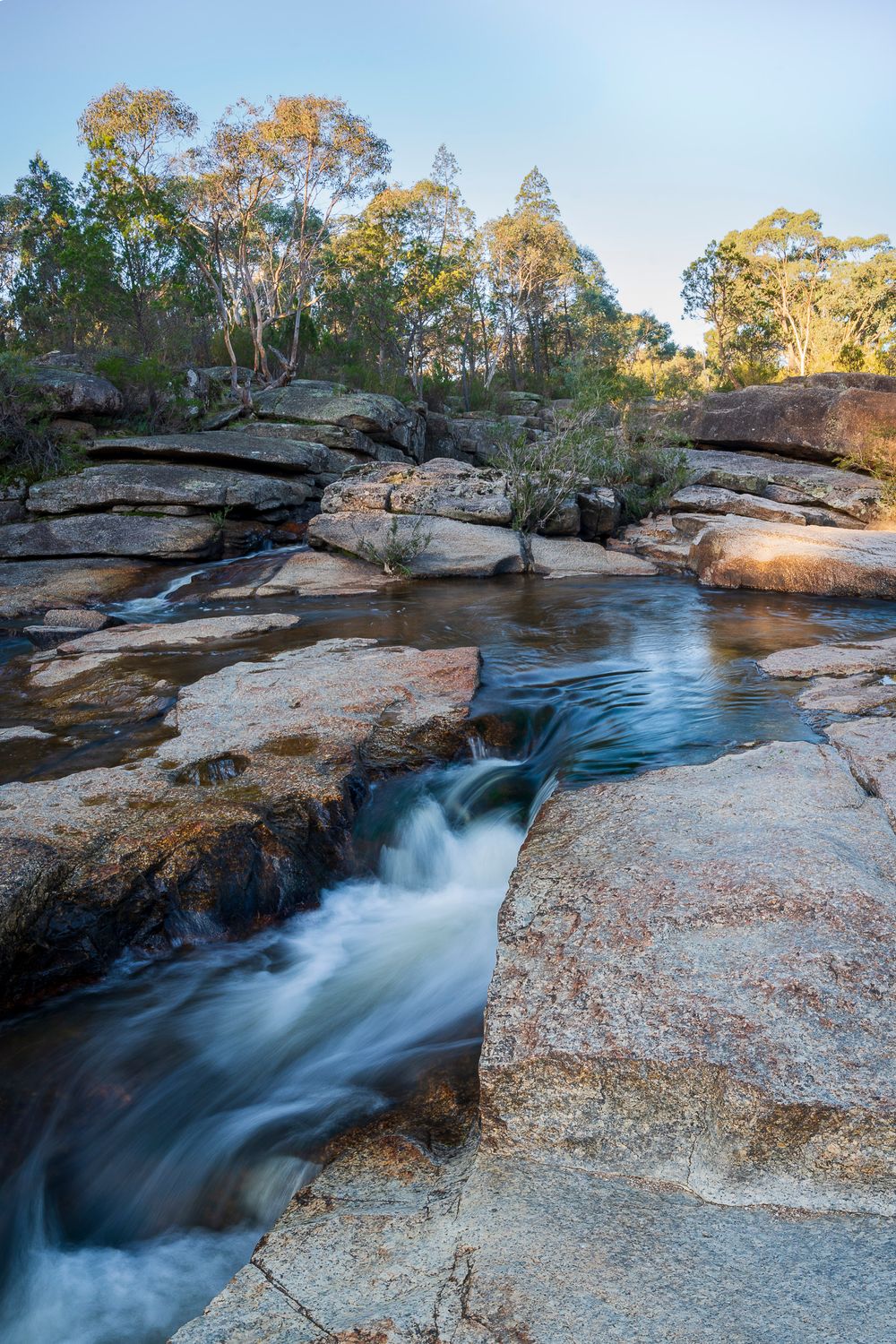 Long exposure waterfall cascading over granite rocks surrounded by eucalyptus trees in Australian bush.