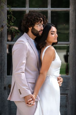 Couple in white and pink attire share intimate moment against architectural backdrop.
