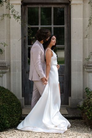 Elegant couple in white attire pose against classic stone building exterior.