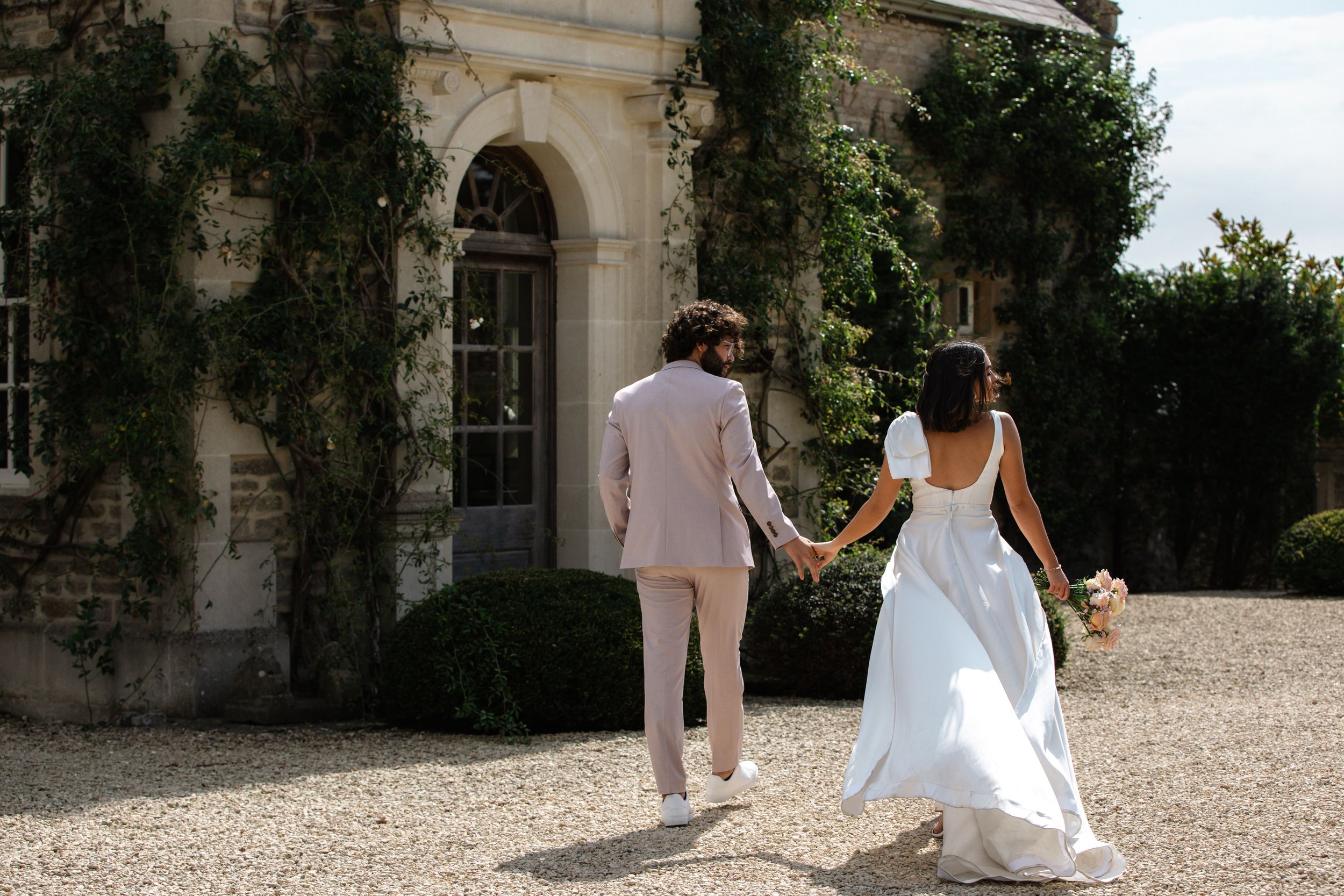 Wedding party members walk along a grand stone building exterior with classic architecture.