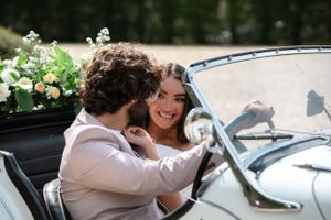 Romantic couple poses in vintage convertible car during wedding photoshoot.
