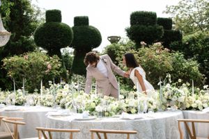 Elegant outdoor wedding reception table setting with white floral arrangements and greenery.