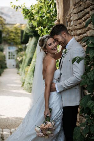 Newlyweds share joyful moments against a rustic stone wall backdrop.