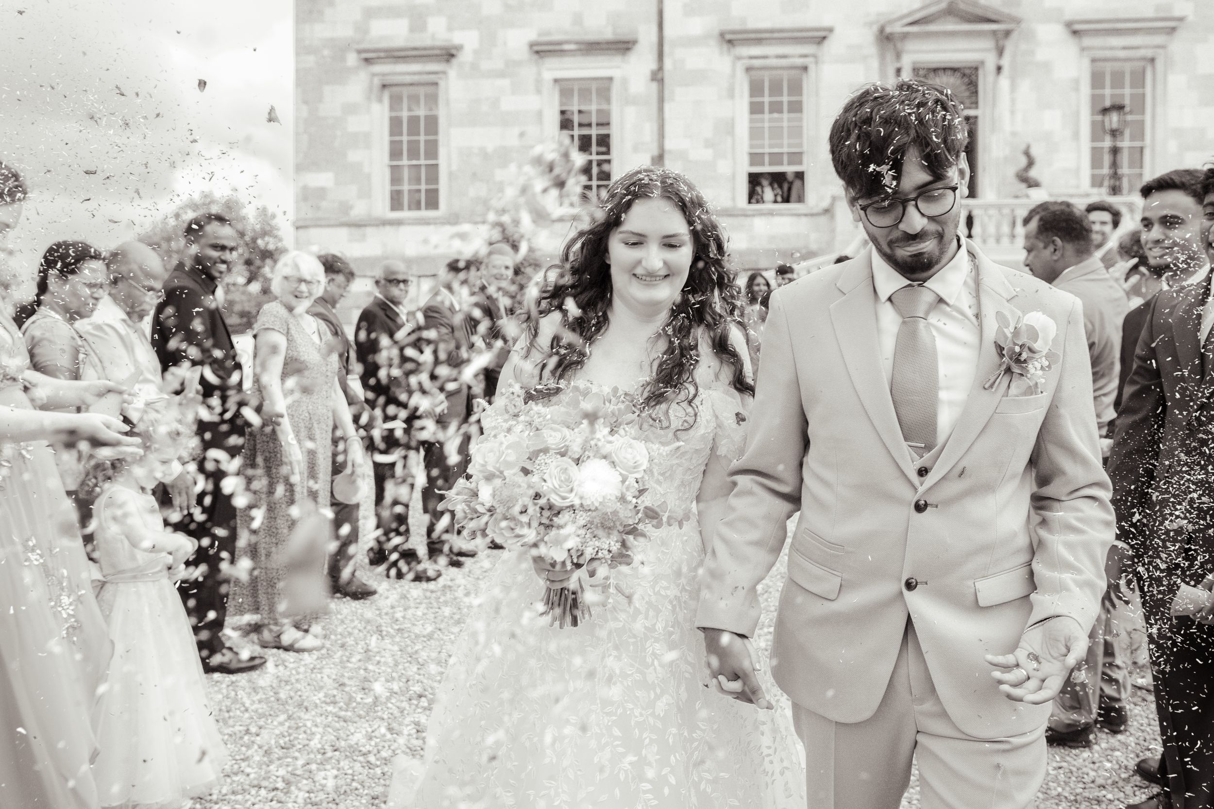 Wedding party celebrates with confetti and joyful laughter outside a grand historic building.