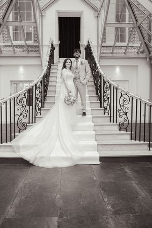Bride in flowing white gown poses on ornate stone steps with wrought iron railings.