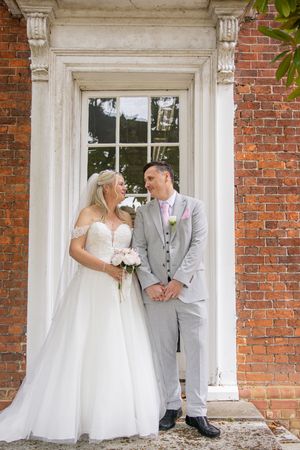 Wedding couple sharing playful moments along classic brick building with white trim.