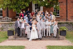 Wedding guests gather outside a traditional red brick building with white trim on a sunny day.