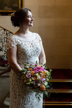 A wedding bouquet with colorful flowers is held against an intricate lace dress.