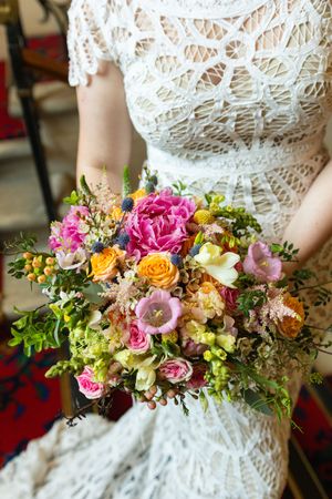 Close-up of a vibrant bridal bouquet featuring pink, orange, and yellow flowers against white lace.
