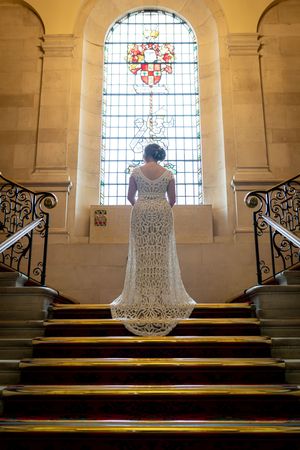 A lace wedding dress is illuminated by stained glass windows in a church sanctuary.