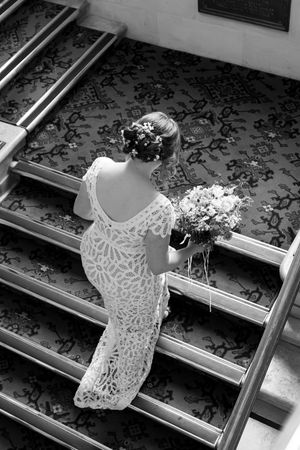 Bride in lace dress looks into ornate mirror during wedding preparations.