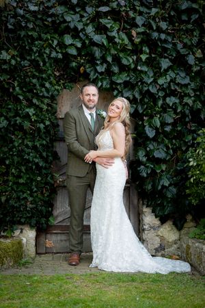 Wedding couple posing against ivy-covered brick wall in garden setting.