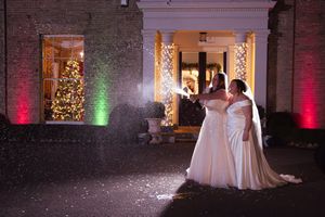 Wedding venue with exposed brick walls illuminated by colorful uplighting and Christmas lights.