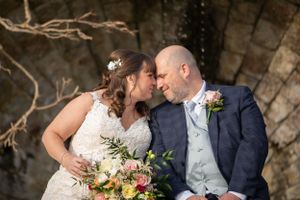 Romantic wedding couple embracing outdoors with floral bouquet.