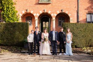 Wedding party gathered outside brick building with hedges.
