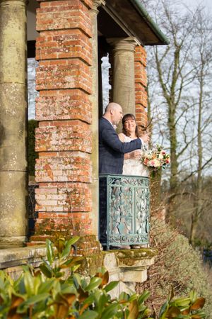 Couple posing on brick terrace with ornate iron railings and columns.