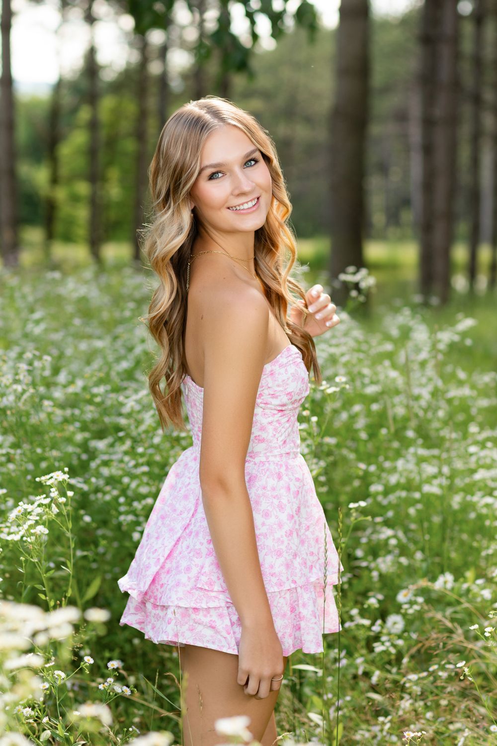 Portrait of person in pink floral dress standing in field of white wildflowers.