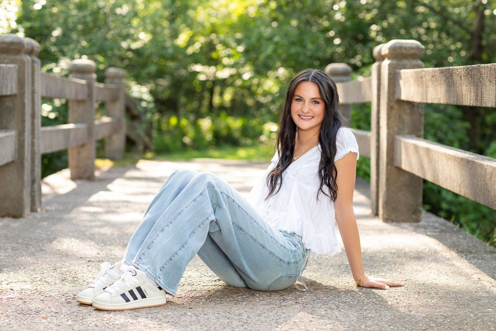 Casual portrait of person in white t-shirt and jeans sitting on wooden bridge.
