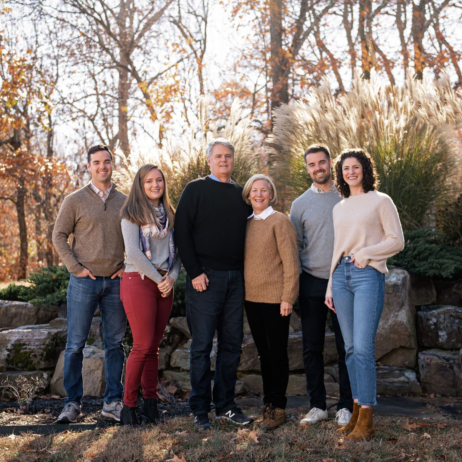 Family group portrait on stone wall with autumn trees in background.