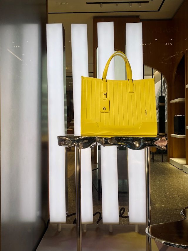 A bright yellow leather handbag displayed on a metal stand against white vertical panels in a retail store display.