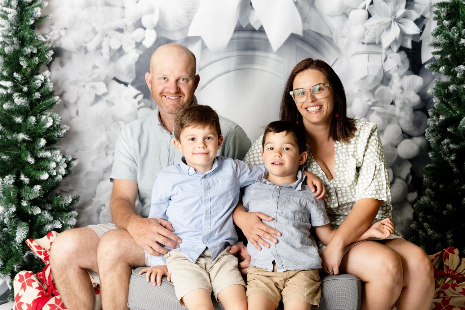 A holiday photo session featuring a family wearing coordinated white outfits against a snowy winter backdrop with greenery.