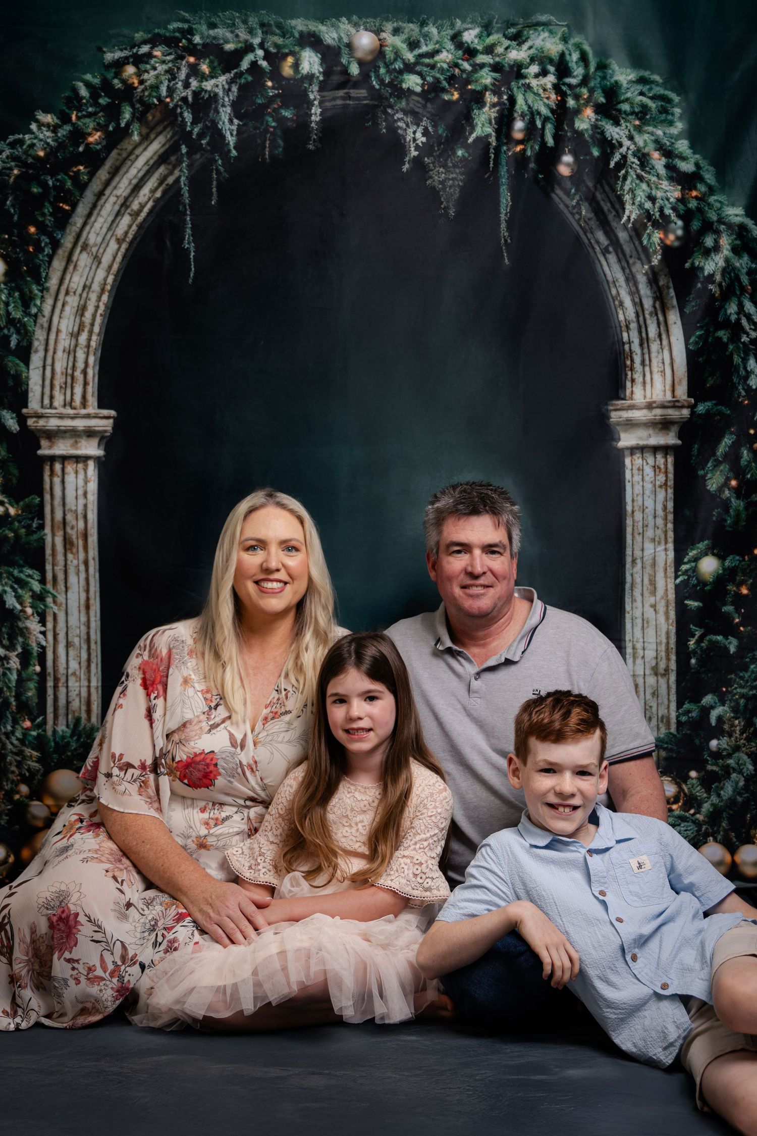 Beautiful family portrait session in front of a floral archway backdrop against a dark moody background.