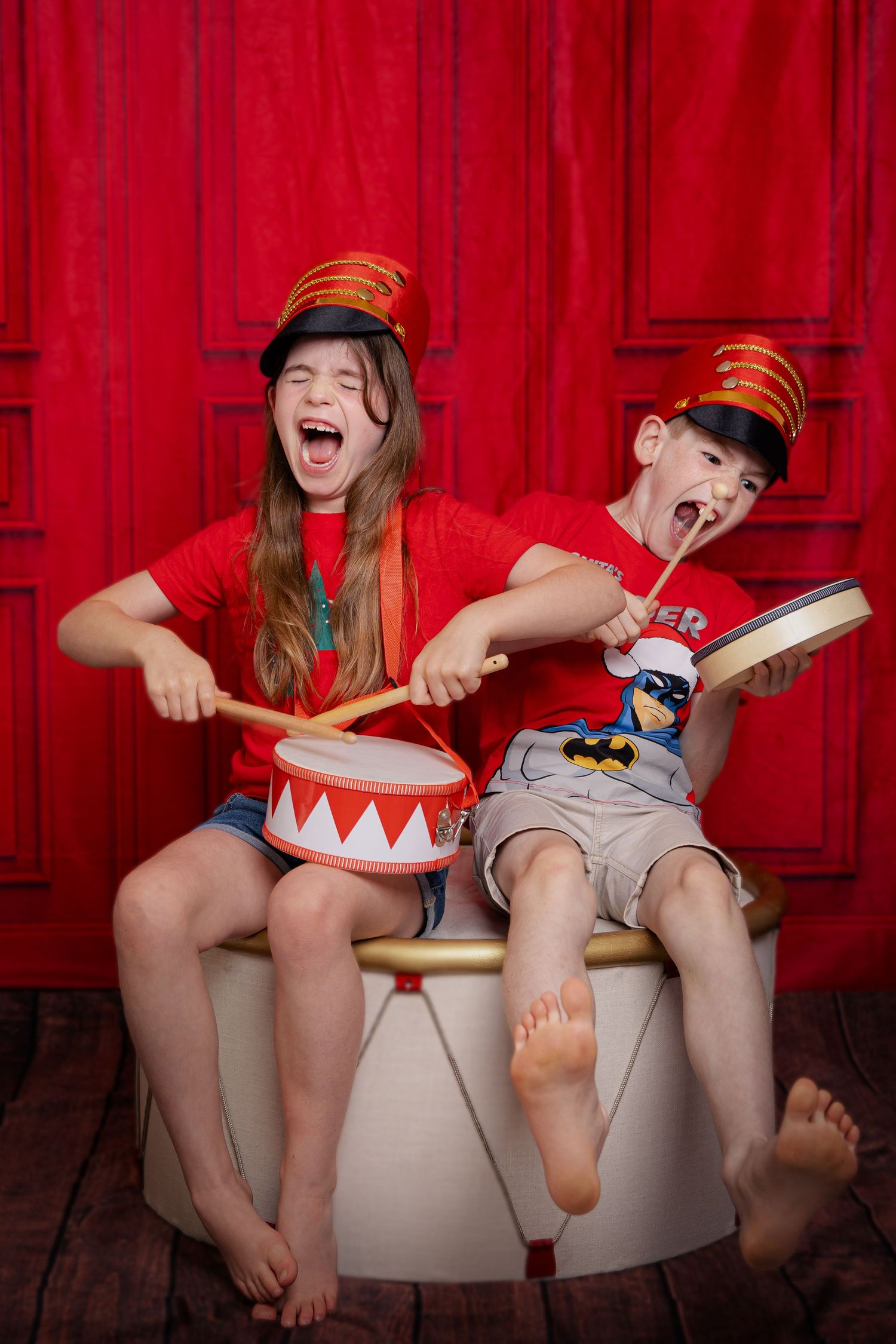 Two giggling children playfully read a book while sitting on white potty training seats against a red backdrop.