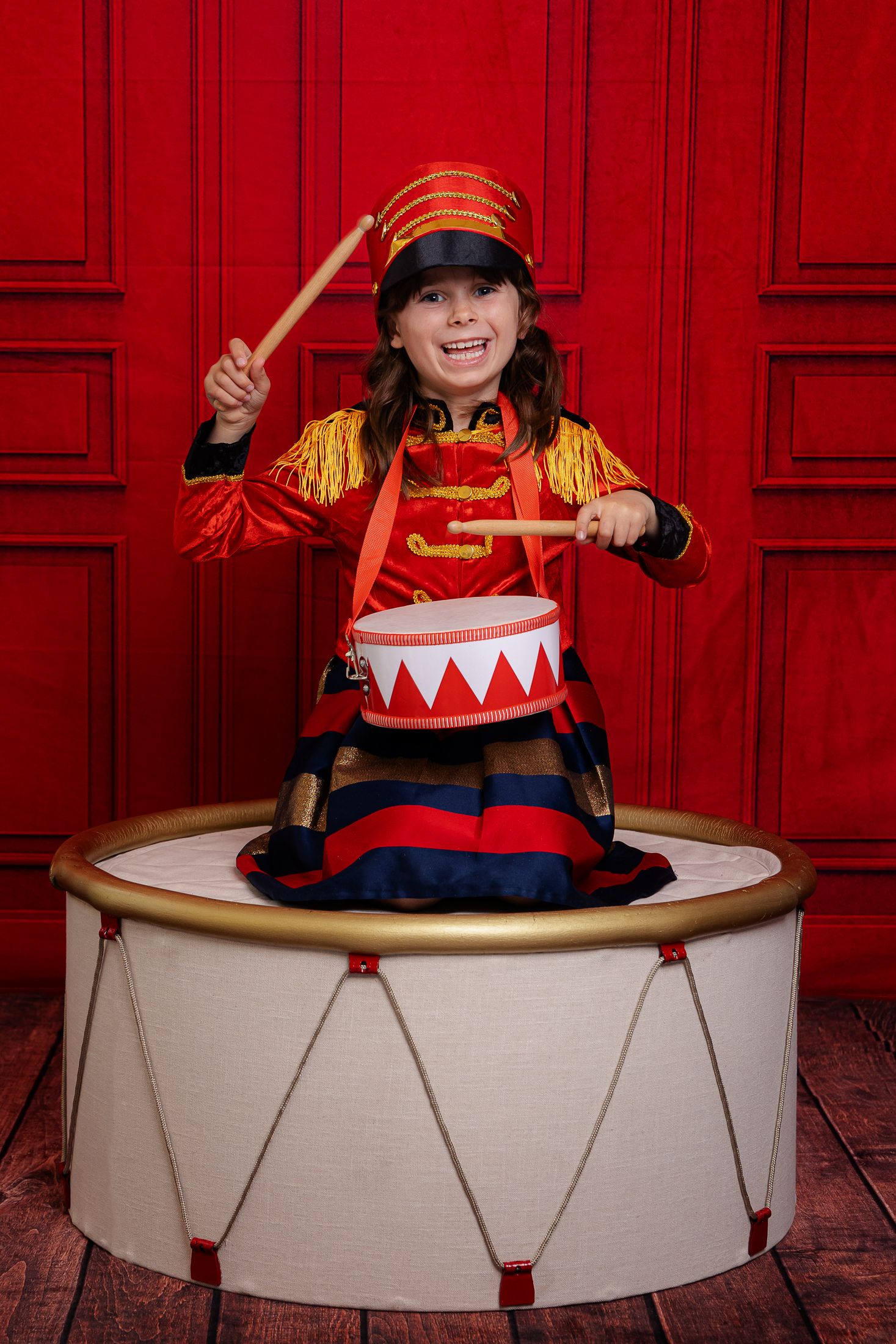 A sequence of four photos showing someone playing in a large white drum against a vibrant red background.