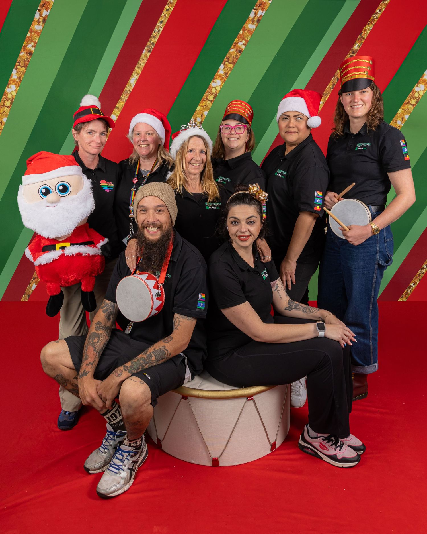 Group of people posing against a festive red and green striped background with glitter and holiday decorations.