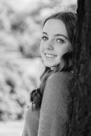 A close-up black and white portrait of a woman smiling next to a tree.