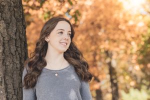 A portrait of a woman with long brown hair standing by a tree in autumn.