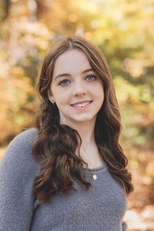 A portrait of a woman in a gray sweater with autumn bokeh background.
