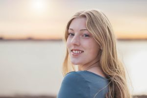 Portrait of someone with blonde hair smiling in front of a sunset waterfront background.