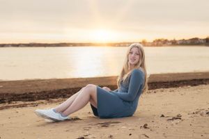 Woman in blue dress sitting on beach at sunset.