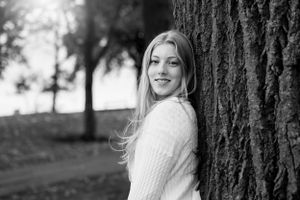 Black and white portrait of woman in sweater by tree trunk.
