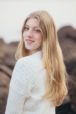 A smiling portrait in a white sweater against a rocky outdoor background.